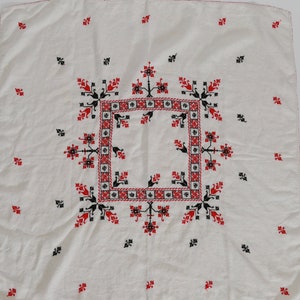 May include: White linen square tablecloth with red and black embroidered floral pattern.