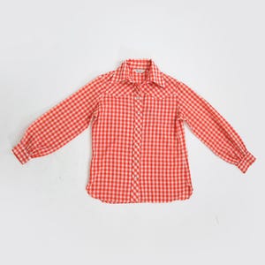 May include: A red and white gingham check shirt with long sleeves. The shirt features a classic collar and buttoned cuffs. The fabric looks lightweight. The shirt is laid flat on a white surface. The shirt is a classic style.