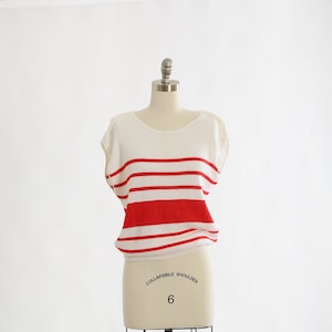 May include: A white and red striped knit top with short sleeves. The top is on a white dress form.