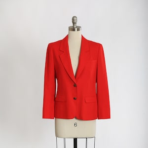 May include: A red blazer with two buttons and a single pocket on each side. The blazer is on a white mannequin.