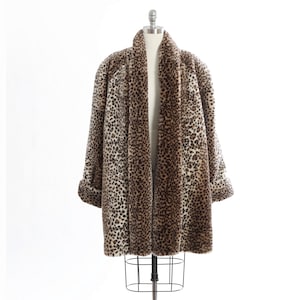 Pode incluir: Um casaco de manga comprida com um padrão de leopardo em tons de castanho, preto e creme. O casaco tem um colarinho largo, uma bainha direita e punhos dobrados nas extremidades das mangas. É exibido num manequim de arame.
