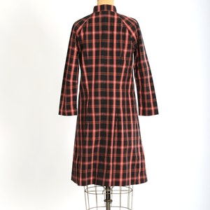 May include: A red and black plaid dress on a mannequin. The dress has a collared neckline and long sleeves.