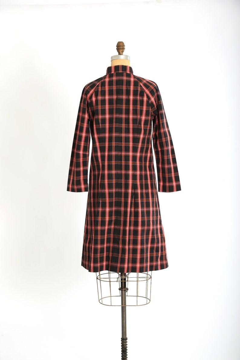May include: A red and black plaid dress on a mannequin. The dress has a collared neckline and long sleeves.