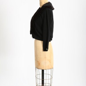 May include: A black cropped cardigan with a brown fur collar. The cardigan is on a dress form.