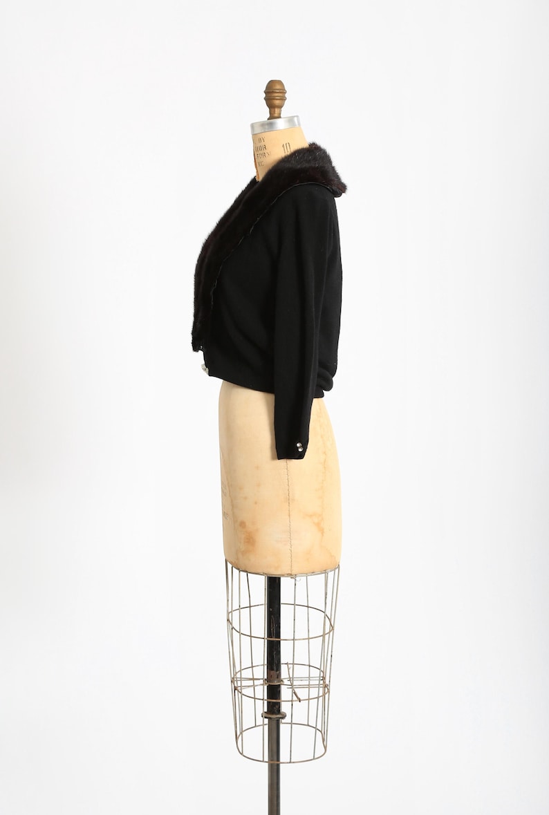 May include: A black cropped cardigan with a brown fur collar. The cardigan is on a dress form.