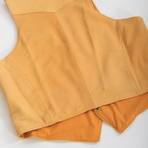 May include: A yellow leather vest with a pointed collar and a button closure. The vest is unlined and has a smooth, soft texture.