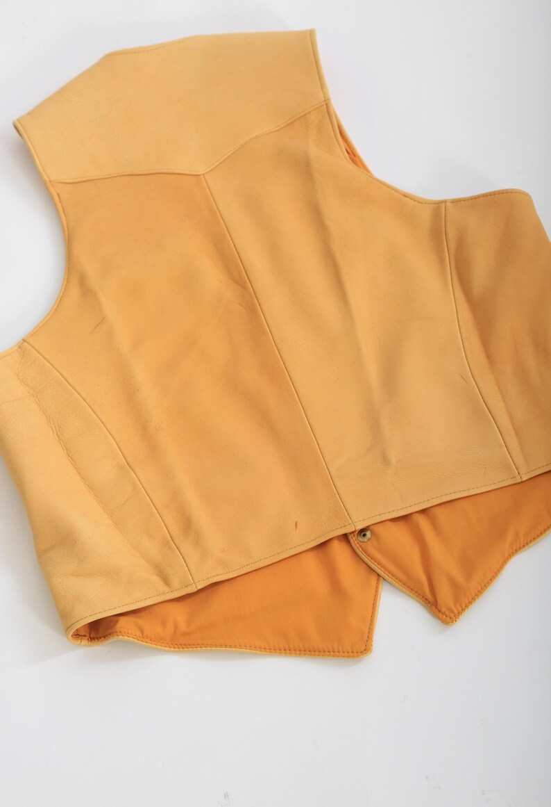 May include: A yellow leather vest with a pointed collar and a button closure. The vest is unlined and has a smooth, soft texture.