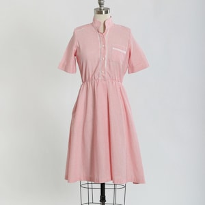 May include: A vintage-style dress in a red and white striped pattern. The dress features a mandarin collar, short sleeves, and a fitted waist that flares into a pleated skirt. It has a small pocket on the chest and is displayed on a mannequin.
