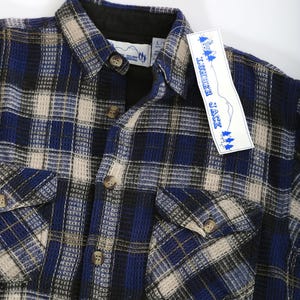 May include: A blue, black, and beige plaid flannel shirt with a woven texture. The shirt has a button-down collar and two chest pockets. The shirt has a "Lumber Jack" tag attached to it.