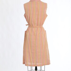 May include: A sleeveless dress with a pink, yellow and green plaid pattern. The dress has a tie belt and pockets.