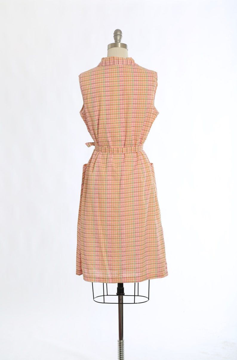 May include: A sleeveless dress with a pink, yellow and green plaid pattern. The dress has a tie belt and pockets.