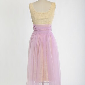 Op de afbeelding: Een vintage jurk zonder mouwen met een geel kanten lijfje en een lavendel tule rok. De jurk heeft een getailleerd lijfje en een volle rok.