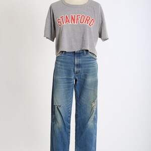 Op de afbeelding: Een grijs gecropped t-shirt met het woord "STANFORD" in rood gedrukt op de voorkant, gecombineerd met een blauwe denim jeans met distressed details.