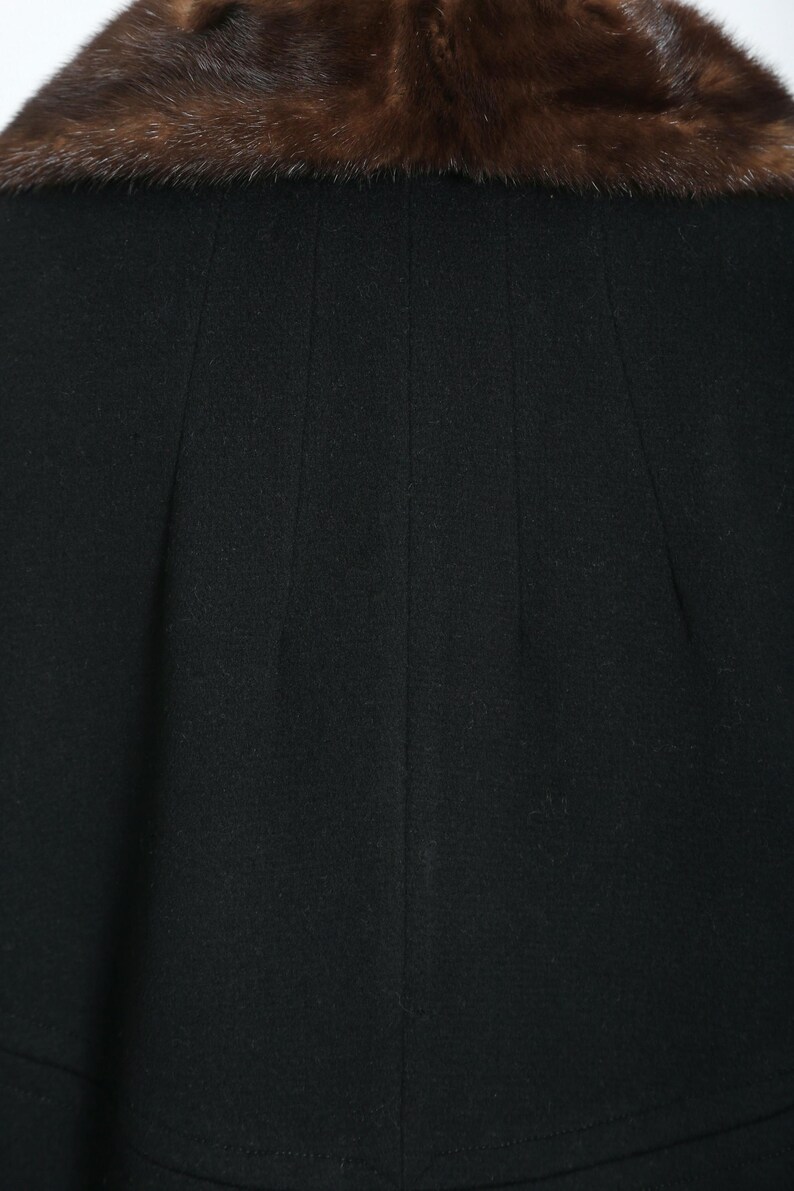 May include: A black coat with a brown fur collar. The coat has a simple design with vertical seams. The fur collar is a rich brown color and adds a touch of luxury to the garment. The coat appears to be made of a soft, warm material.
