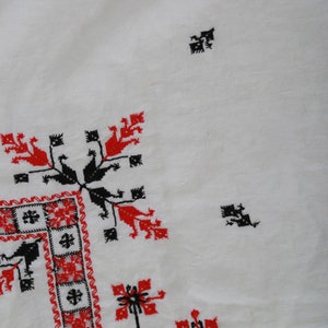 May include: White fabric with red and black embroidered designs. The design features a repeating pattern of stylized flowers and geometric shapes.