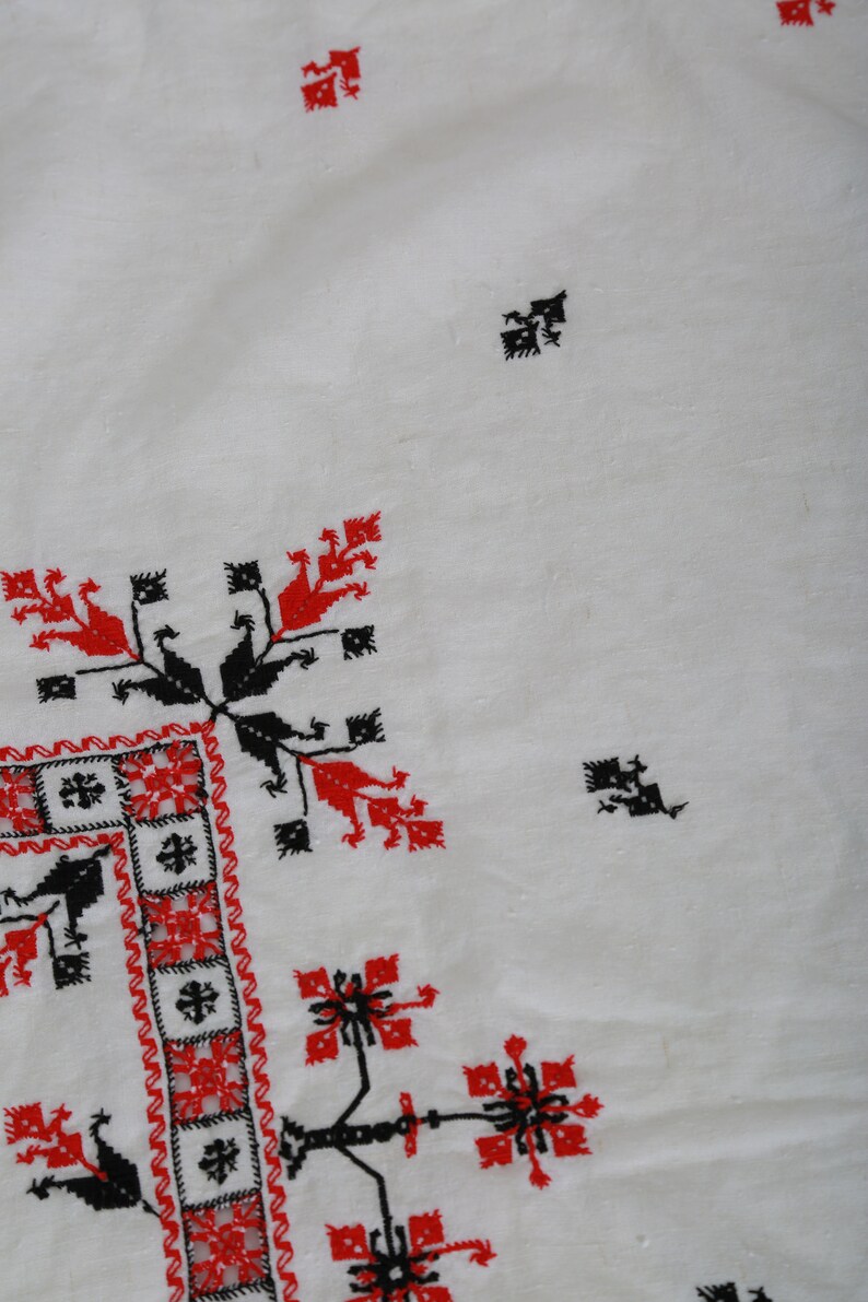 May include: White fabric with red and black embroidered designs. The design features a repeating pattern of stylized flowers and geometric shapes.