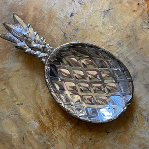 May include: A silver pineapple-shaped serving dish with a textured, diamond-shaped pattern. The dish is made of metal and has a realistic pineapple design.
