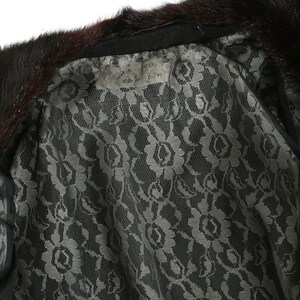 May include: A black fur collar with a black lace lining. The lining has a floral pattern. A white tag is attached to the collar with the text "Genuine Mink Fur" written on it.
