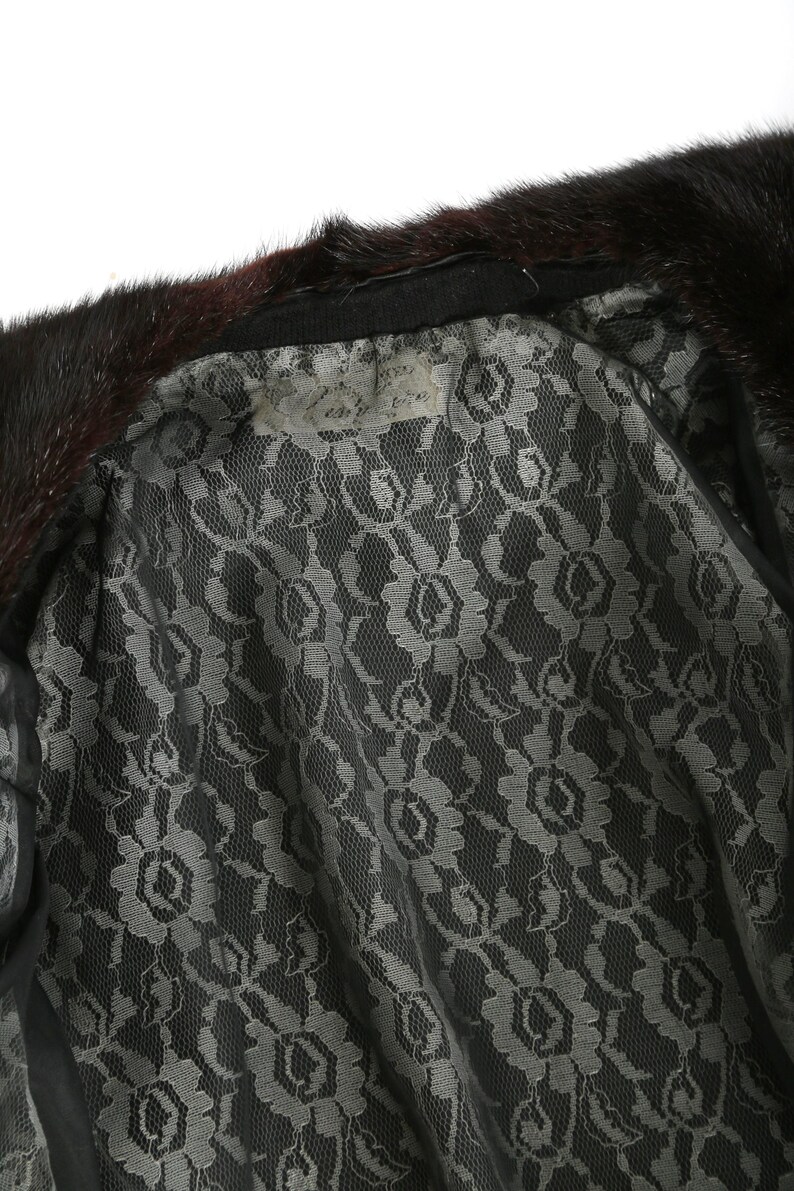 May include: A black fur collar with a black lace lining. The lining has a floral pattern. A white tag is attached to the collar with the text "Genuine Mink Fur" written on it.