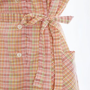 May include: A pink and yellow gingham dress with a self-tie belt and a patch pocket. The dress has a button-up front.