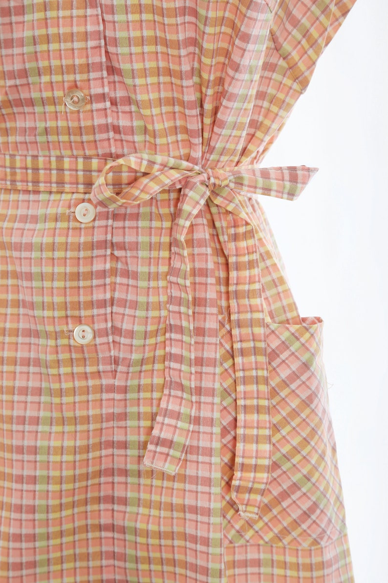 May include: A pink and yellow gingham dress with a self-tie belt and a patch pocket. The dress has a button-up front.