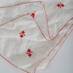 May include: White linen fabric with red embroidered floral designs. The fabric is folded in half and has a red stitched border.