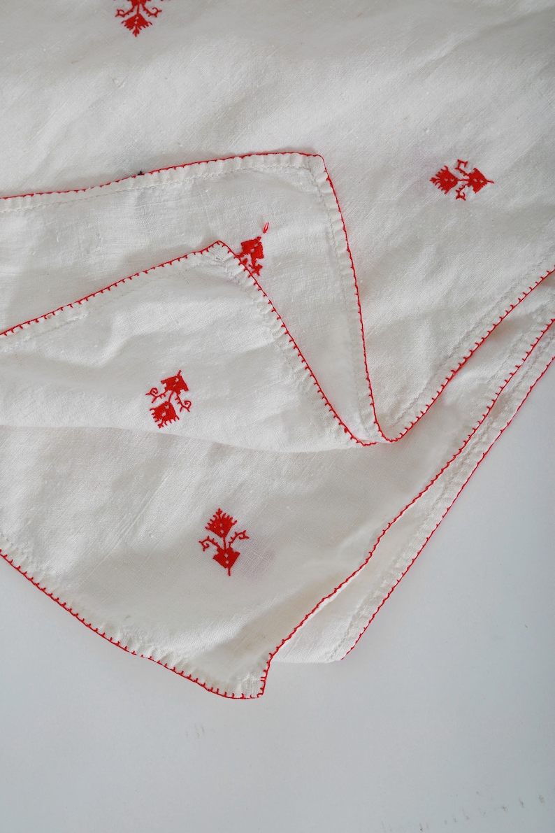 May include: White linen fabric with red embroidered floral designs. The fabric is folded in half and has a red stitched border.