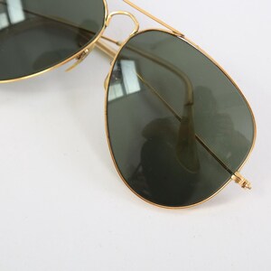 May include: Aviator sunglasses featuring a thin gold-tone metal frame and dark green teardrop-shaped lenses. The design includes a double bridge across the top and slender temples, providing a classic look with a metallic finish and tinted glass.