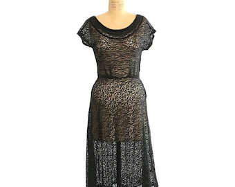 May include: A vintage black lace dress with a scoop neckline and short sleeves. The dress is fitted at the waist and flares out to a midi length. It is displayed on a dress form.