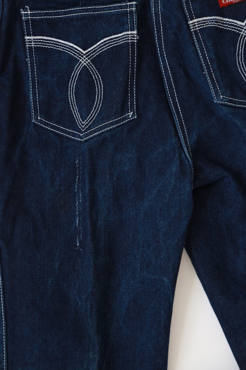 May include: A pair of dark blue denim jeans with white stitching detail on the back pockets.