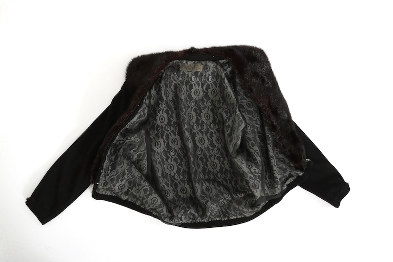 May include: A black fur-trimmed jacket with a black and white patterned lining. The jacket is unzipped and laid flat.