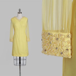 May include: A yellow vintage dress with long sheer sleeves and beaded trim. The dress has a simple, fitted silhouette and a scoop neckline.