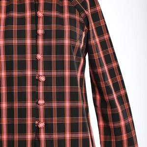 May include: A black and pink plaid shirt with a mandarin collar and button closure. The shirt has long sleeves and a relaxed fit.