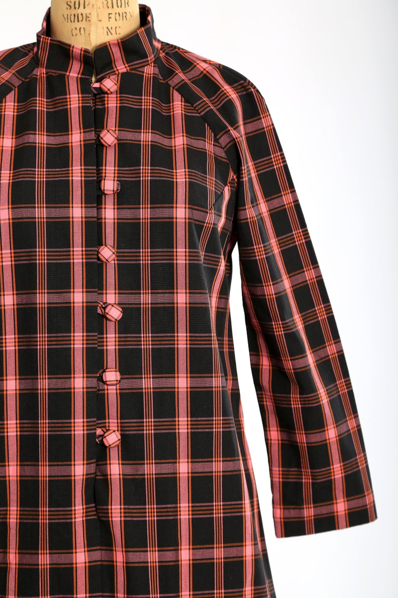 May include: A black and pink plaid shirt with a mandarin collar and button closure. The shirt has long sleeves and a relaxed fit.