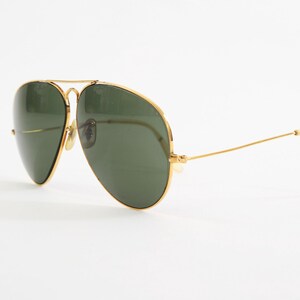 May include: Aviator sunglasses featuring a thin gold metal frame and dark green teardrop-shaped lenses. The design includes a double bridge across the top and slender gold temples with curved ends, providing a classic look with a metallic finish.