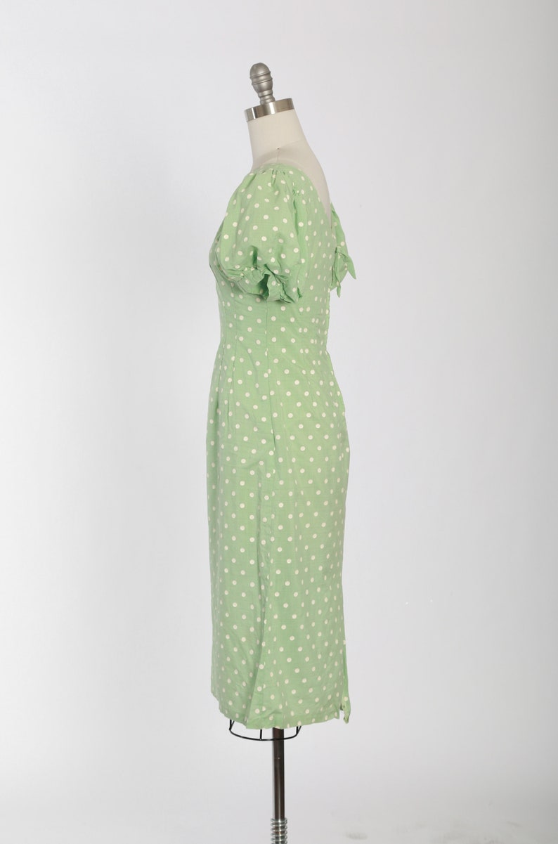 May include: A green dress with white polka dots and short puffed sleeves. The dress is fitted and has a scoop neckline.