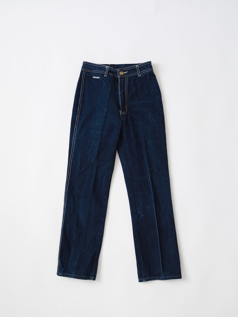 May include: A pair of dark blue denim jeans with a high waist and straight legs. The jeans have a white stitching detail along the seams.