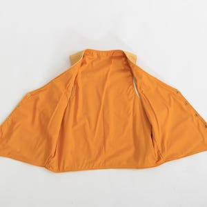 May include: A yellow sleeveless vest with a snap closure. The vest is made of a soft, lightweight fabric and has a relaxed fit.