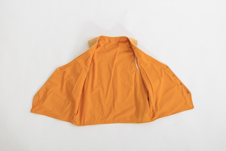 May include: A yellow sleeveless vest with a snap closure. The vest is made of a soft, lightweight fabric and has a relaxed fit.