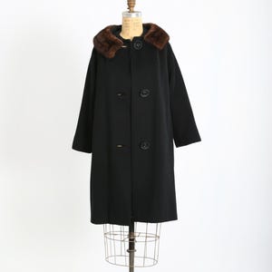May include: A vintage black wool coat with a brown fur collar. The coat has a classic design with large buttons and a tailored fit. It is displayed on a dress form against a white background. The coat is a timeless piece of outerwear.