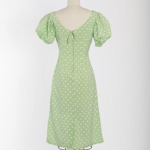 May include: A green dress with white polka dots and a back zipper. The dress has puffed sleeves and a V-neckline.