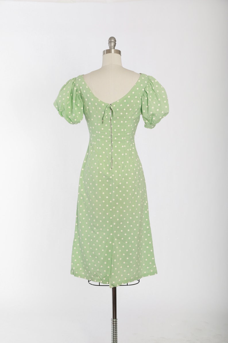 May include: A green dress with white polka dots and a back zipper. The dress has puffed sleeves and a V-neckline.