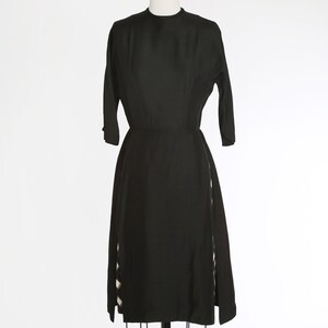 Puede incluir: Un vestido negro con un corpi&ntilde;o ajustado y una falda completa. La falda tiene dos paneles laterales con un patr&oacute;n geom&eacute;trico blanco y negro.