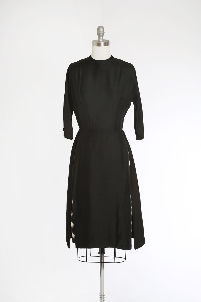 Puede incluir: Un vestido negro con un corpi&ntilde;o ajustado y una falda completa. La falda tiene dos paneles laterales con un patr&oacute;n geom&eacute;trico blanco y negro.