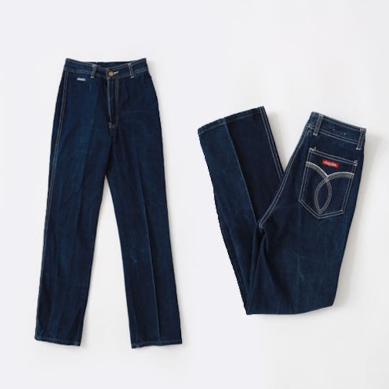May include: Two pairs of blue denim jeans. One pair has a high waist and straight legs. The other pair has a lower waist and a more relaxed fit.
