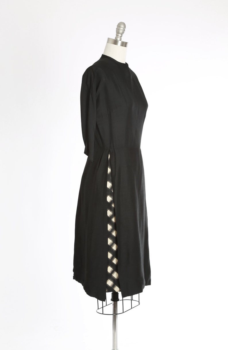 Puede incluir: Un vestido negro con una abertura lateral y un patr&oacute;n a cuadros blanco y negro debajo.