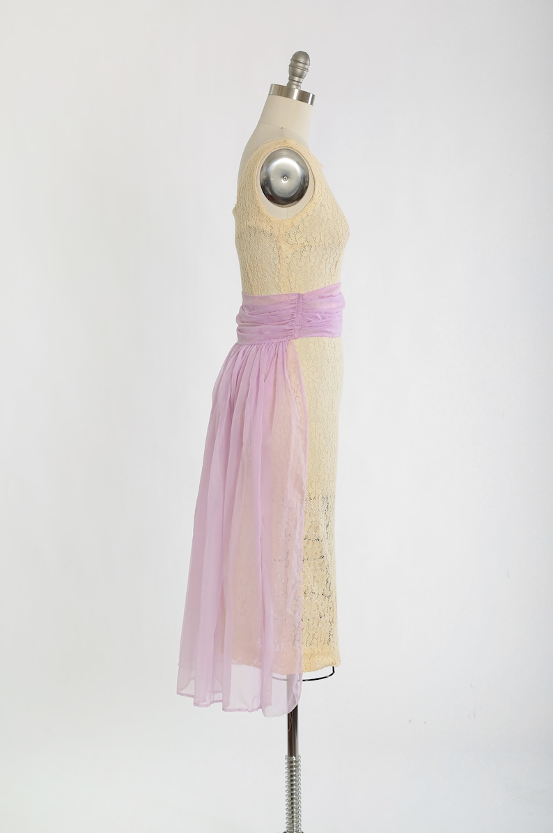 Op de afbeelding: Een vintage-stijl jurk met een cr&egrave;mekleurige kantboord en een lavendelkleurige chiffonrok. De jurk heeft een aansluitend lijfje en een zwierige rok.