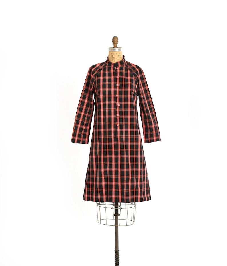 May include: A black and red plaid dress with a mandarin collar and button closure. The dress is on a mannequin.