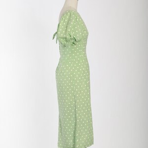 May include: A green midi dress with white polka dots and a puff sleeve. The dress has a tie detail at the back.