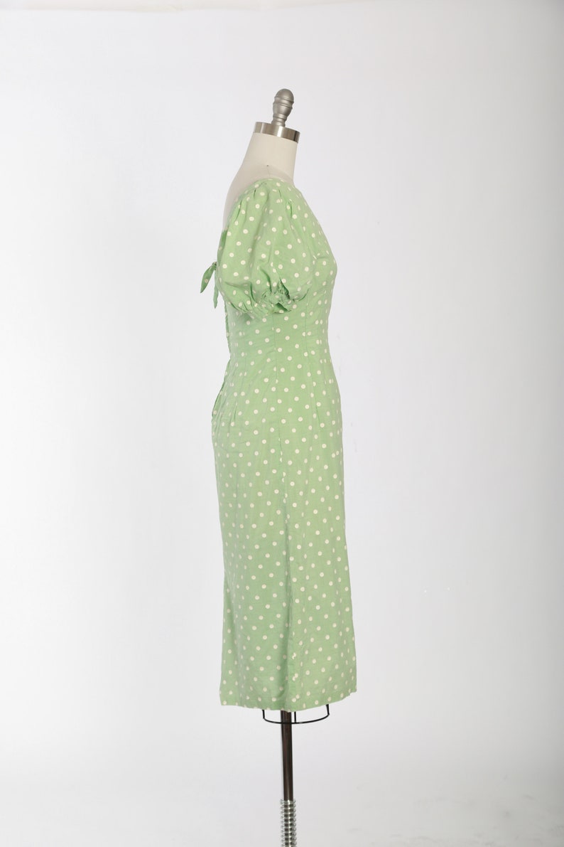 May include: A green midi dress with white polka dots and a puff sleeve. The dress has a tie detail at the back.